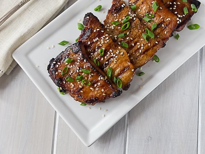 a white plate of grilled korean pork chops topped with sesame seeds and green onions