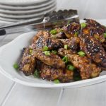 a white plate of thai chicken wings with tongs