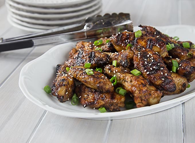 a white plate of thai chicken wings with tongs