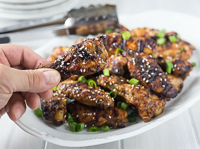 a plate of grilled thai chicken wings with a hand holding one in front