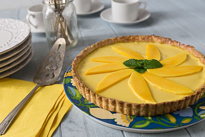 mango passionfruit tart on a colored plate with coffee in the back