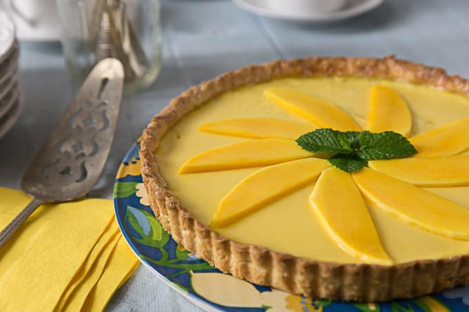 a mango passionfruit tart with mint leaves and yellow napkins and a cake knife on the left