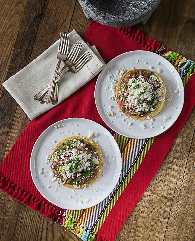 two white plates with tostadas on a red placemat with forks and a napkin on the left