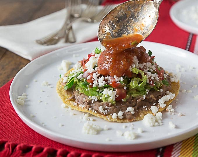 a tostada on a white plate with a spoon adding sauce