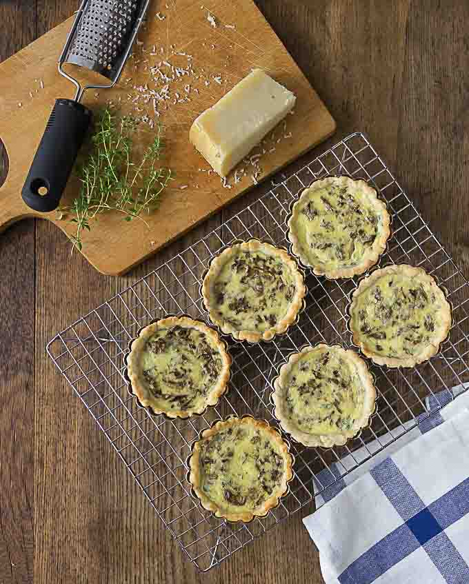 mushroom tarts on a rack next to a cutting board with cheese and thyme