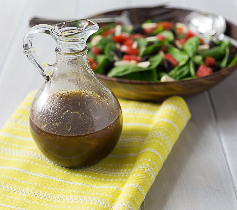 a jug of balsamic dressing on a yellow napkin with a salad in the back