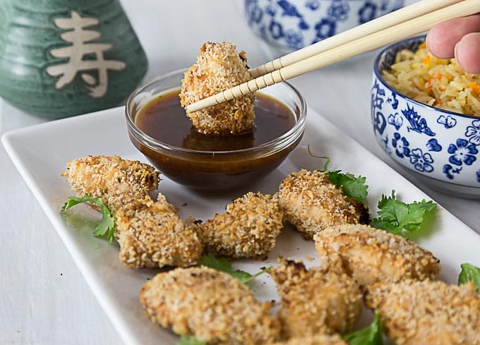 A white plate with baked chicken tenders and a pair of chopsticks dipping into sauce.