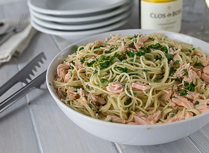 a white bowl of angel hair pasta with salmon pieces and parsley
