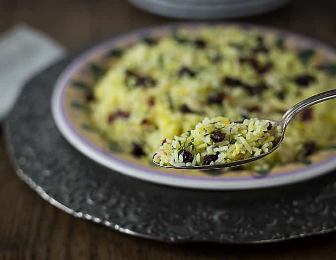 a spoonful of saffron rice with dried cranberries with a plate in the back