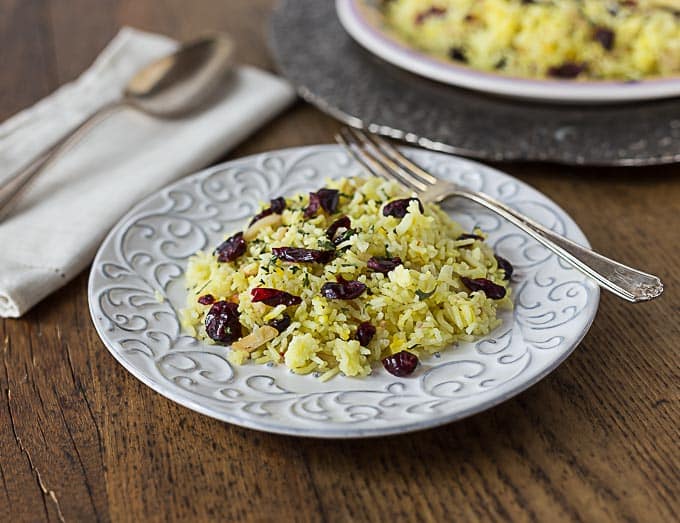 saffron rice with craisins on a white plate with a fork and a spoon and napkin on the left