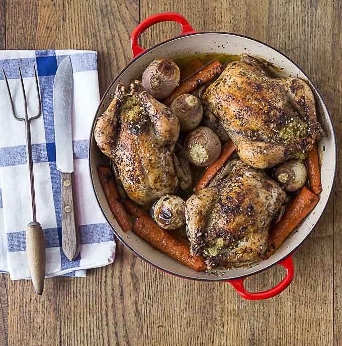 roasted cornish hens, carrots, and potatoes in a dutch oven with a fork and knife on the left 