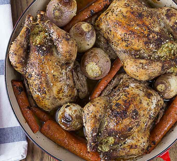 a closeup of roasted cornish hens, carrots, and potatoes with a blue and white napkin on the left