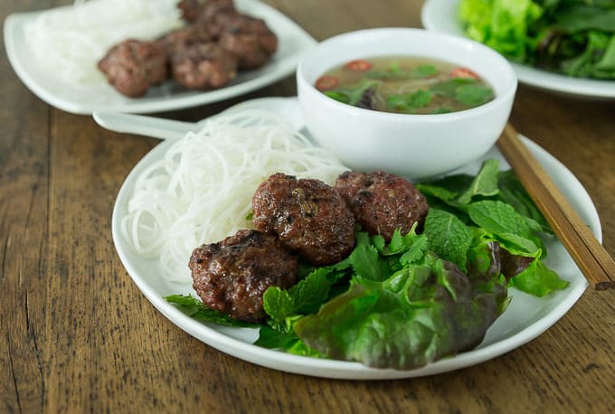 a plate of vietnamese rice noodles, meatballs, salad greens, and broth