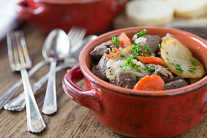a red bowl of french beef stew with forks and spoons on the left