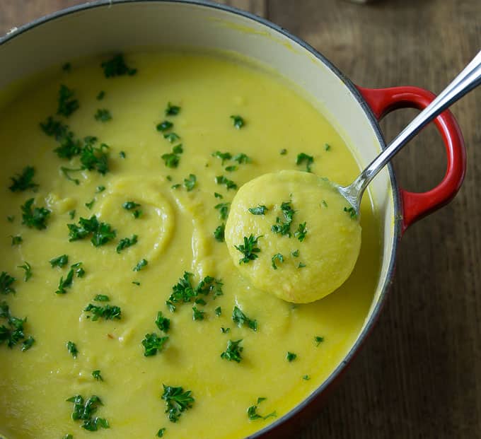 a dutch oven filled with cauliflower soup with parsley and a ladle 