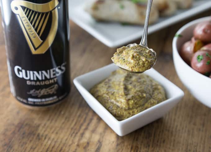 a can of guinness and a bowl of mustard with a spoon scooping mustard
