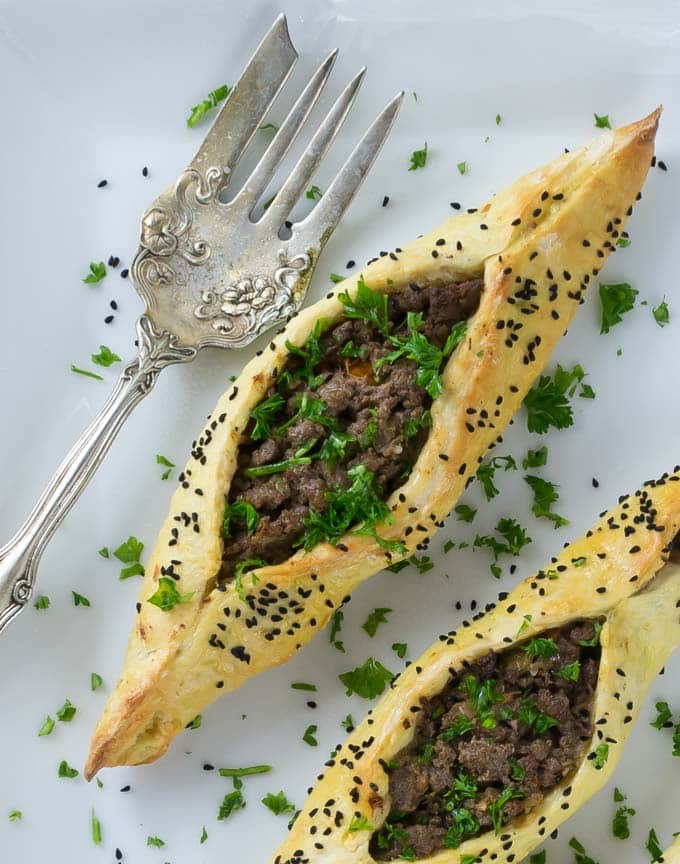 two lamb fatayer on a white plate with parsley and a fork on the left