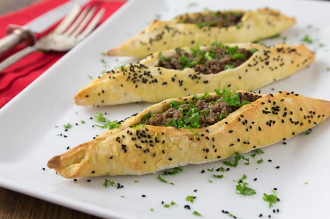 three lamb fatayer on a white plate with nigella seeds and parsley 