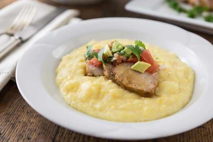 a white bowl of grits with sliced pork