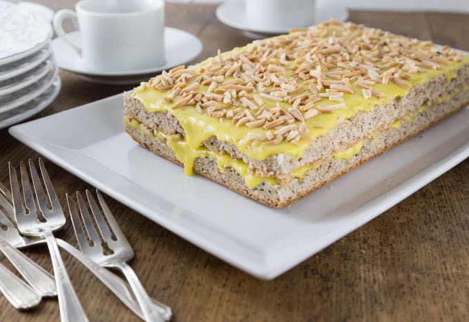 a slab of almond cake with yellow frosting and almond pieces and forks on the left