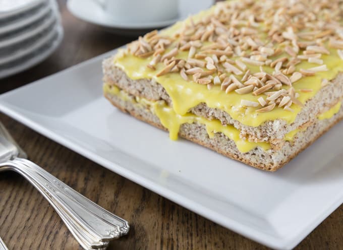 a white plate with Swedish almond cake with yellow frosting and almond pieces