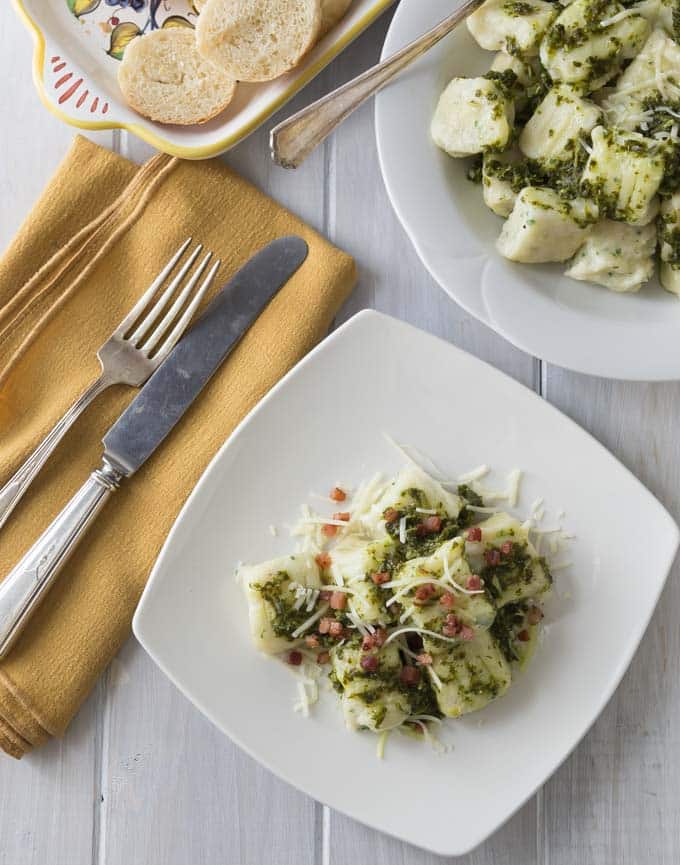 a plate of ricotta gnocchi with pesto and bacon with the main serving dish in the top right
