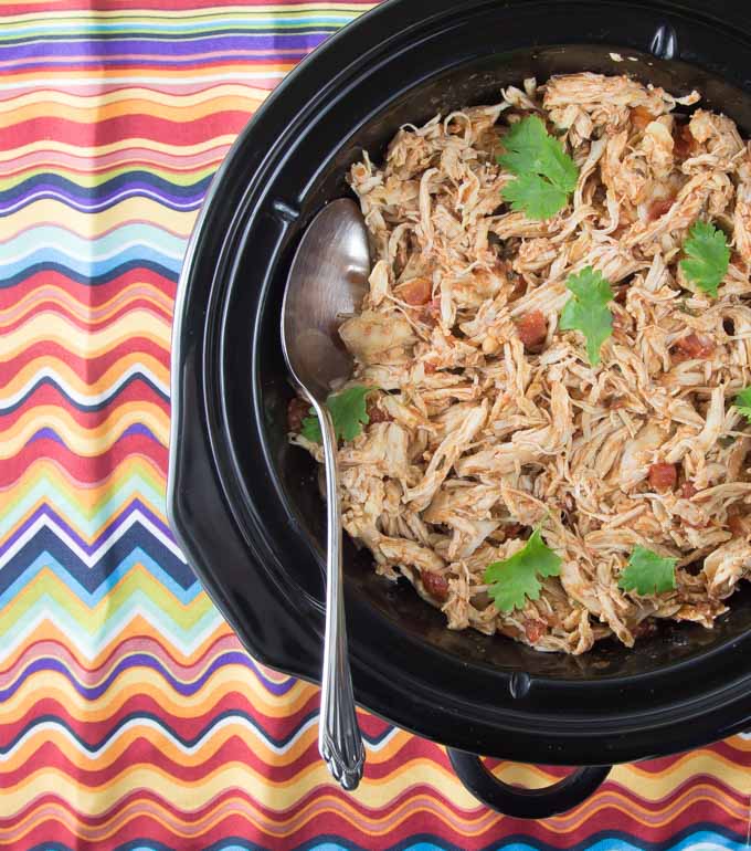 chicken tinga in the slow cookers with a spoon on a colorful napkin 