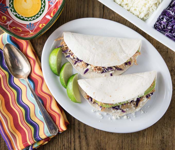 two tacos on a plate with lime wedges next to a striped napkin with a spoon