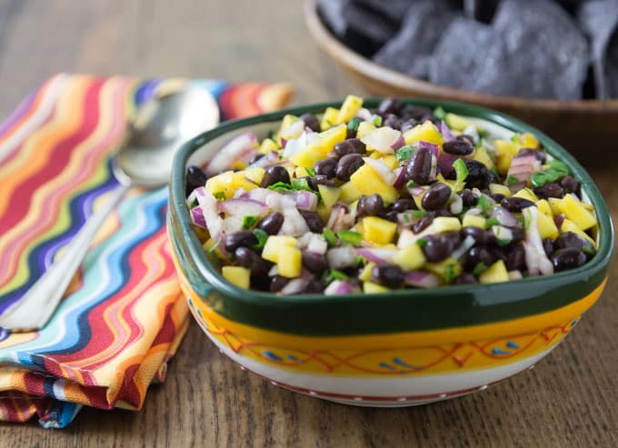 a bowl of mango black bean salsa with a striped napkin and a spoon on the left