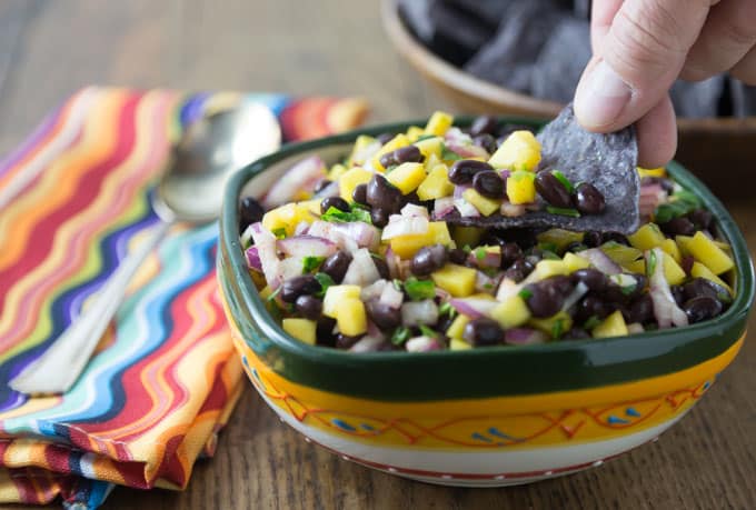 a chip scooping mango black bean salsa with a striped napkin and a spoon on the left