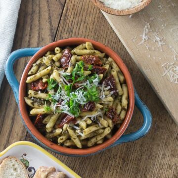 A blue bowl with penne pasta, sun dried tomato, parsley and grated cheese.