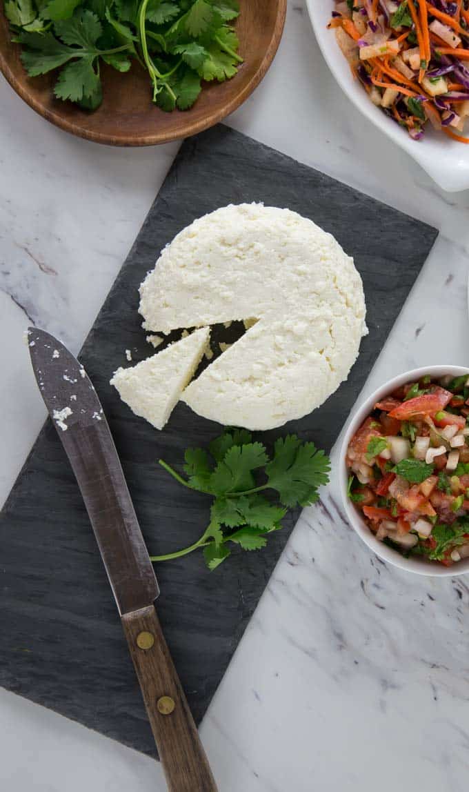 a black slate with farmers cheese sliced and some cilantro with bowls of slaw and more cilantro