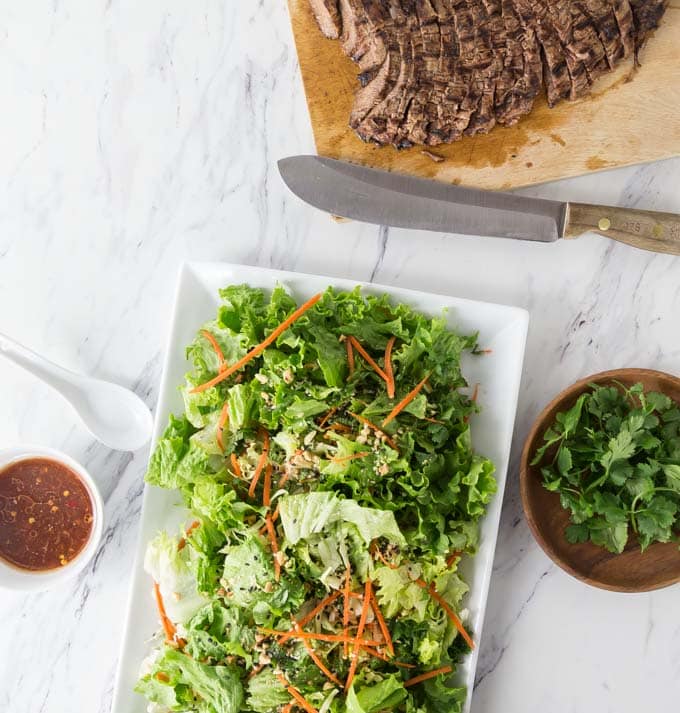 a salad and a cutting board of beef with a knife 