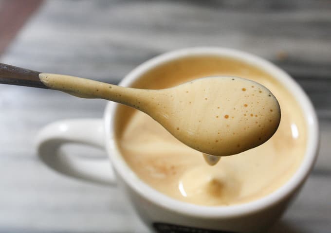 a cup of egg coffee and a spoon of foam