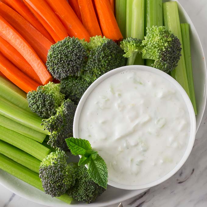 A white bowl with Greek tzatziki along with sliced carrots and celery.
