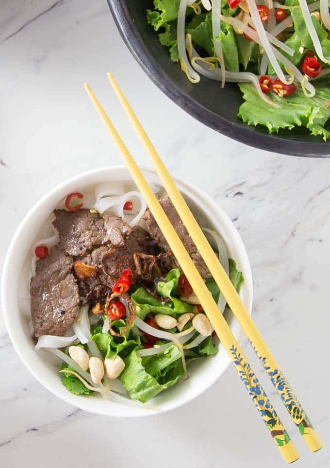 a close up of pho salad with yellow chopsticks and a serving dish above 