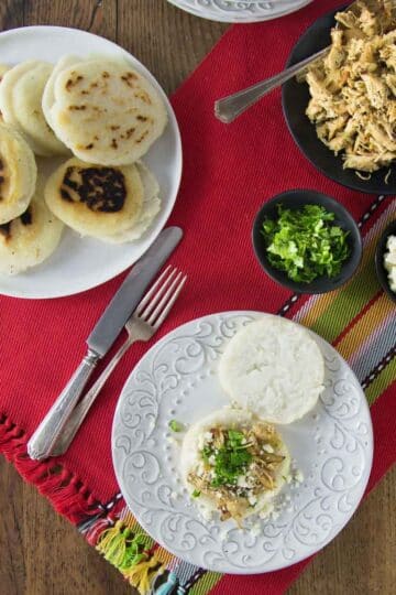 An overhead photo of arepas on a white plate with shredded chicken.