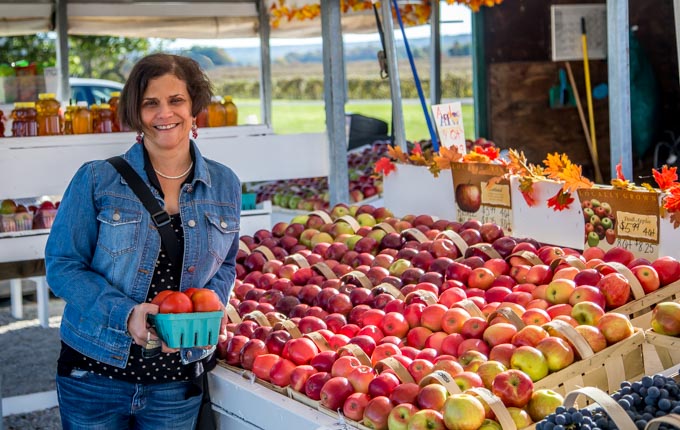 a lady buying apples at a farm stand with baskets of apples on the right 