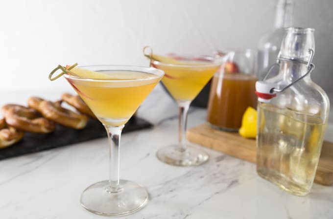 two apple cider martinis with pretzels in the back and syrup on the right