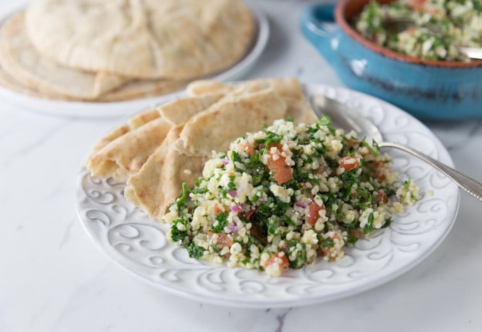 a white plate with tabouleh and pita 