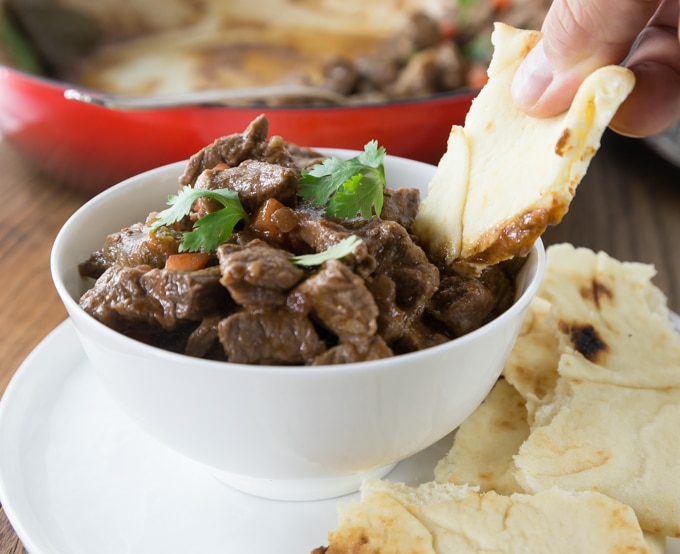 a bowl of lamb stew with naan dipping in and naan on the saucer
