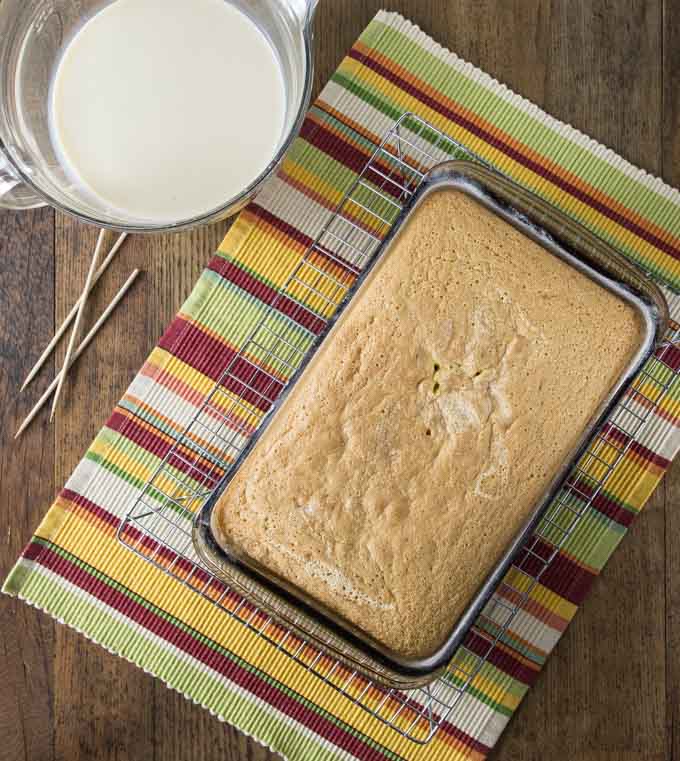 an unfrosted cake on a drying rack on a placemat next to a bowl of creme and toothpicks