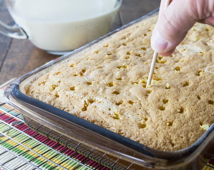 hands poking holes into an unfrosted cake