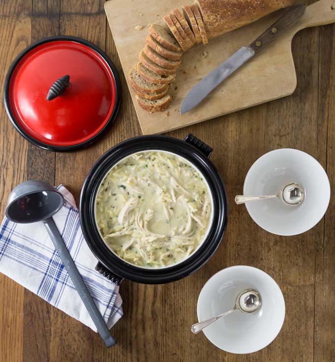 a dutch oven filled with chicken soup and sliced bread and two spoons in bowls on the right