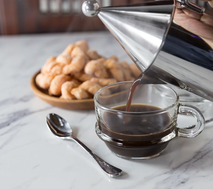 a glass mug of coffee being poured with a spoon on the left