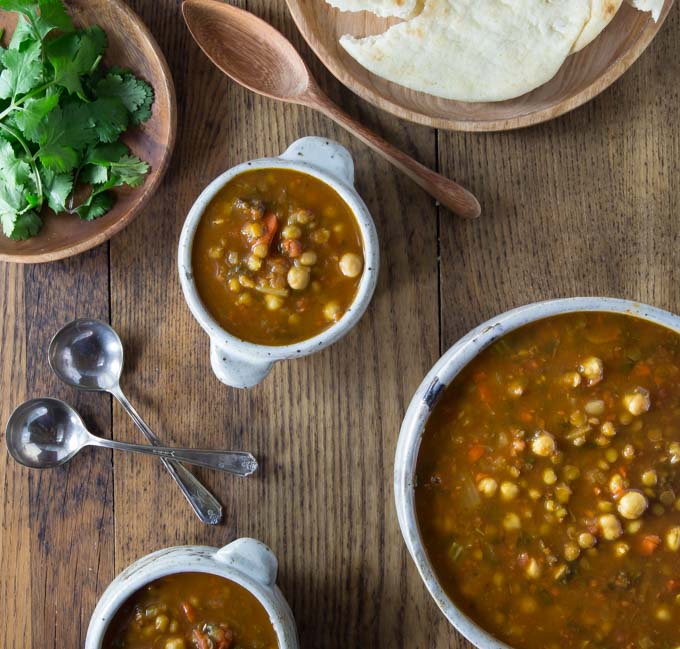 a pot of moroccan lentil soup, two bowls of soup, a plate of cilantro and a plate of naan