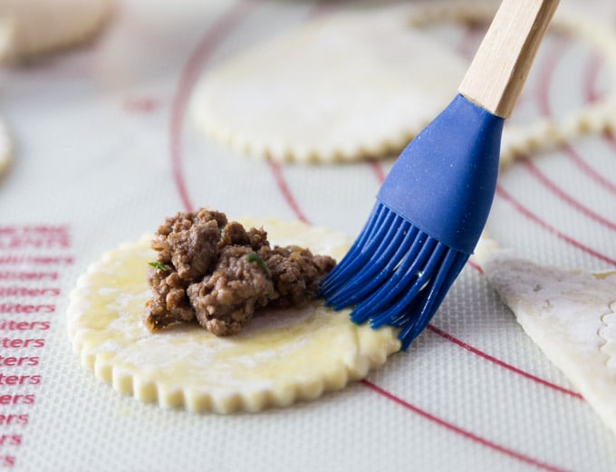 a pastry brush adding butter to a circle of puff pastry with beef