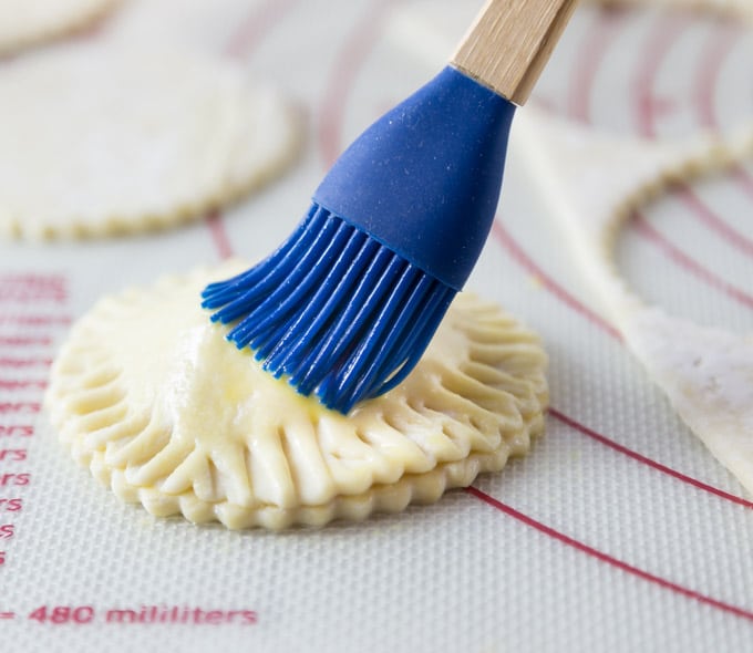 a pastry brush adding butter to the outside of an unbaked beef pastry