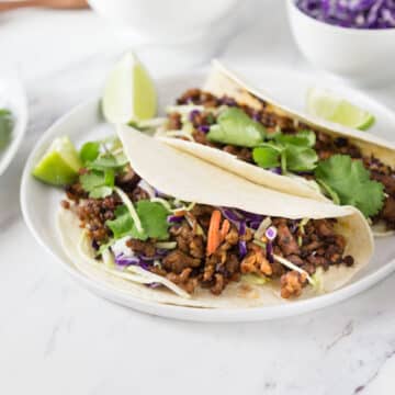 Pork tacos on a white plate with red cabbage in the background.
