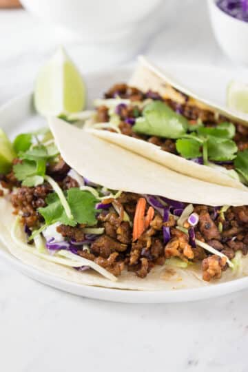 Pork tacos on a white plate with red cabbage in the background.